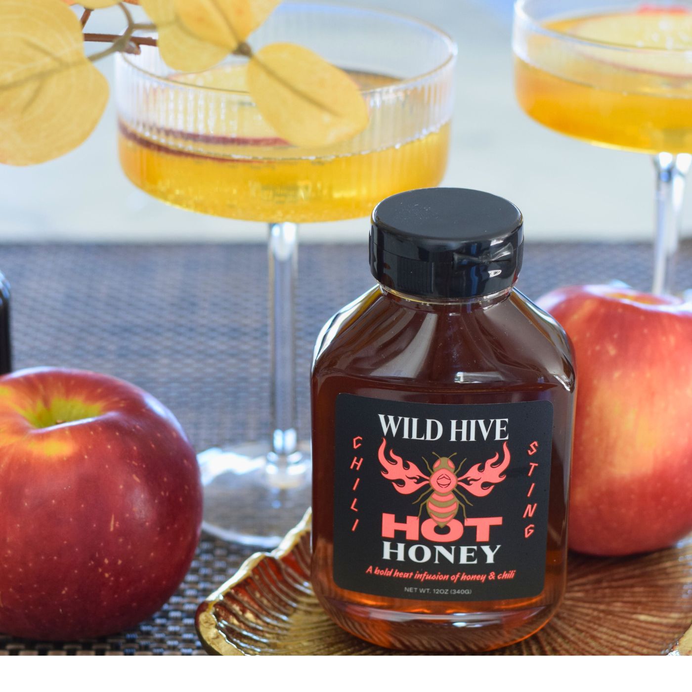 Bottle of Wild Hive Chili Sting Hot Honey with apples and fall mocktails/cocktails in the background