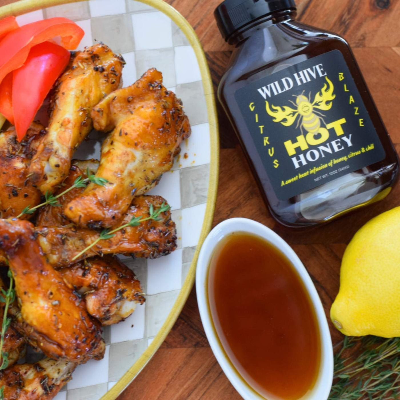 Baked chicken wings with herbs and Wild Hive Citrus Blaze on a wood table. Lemon and thyme are also featured. 