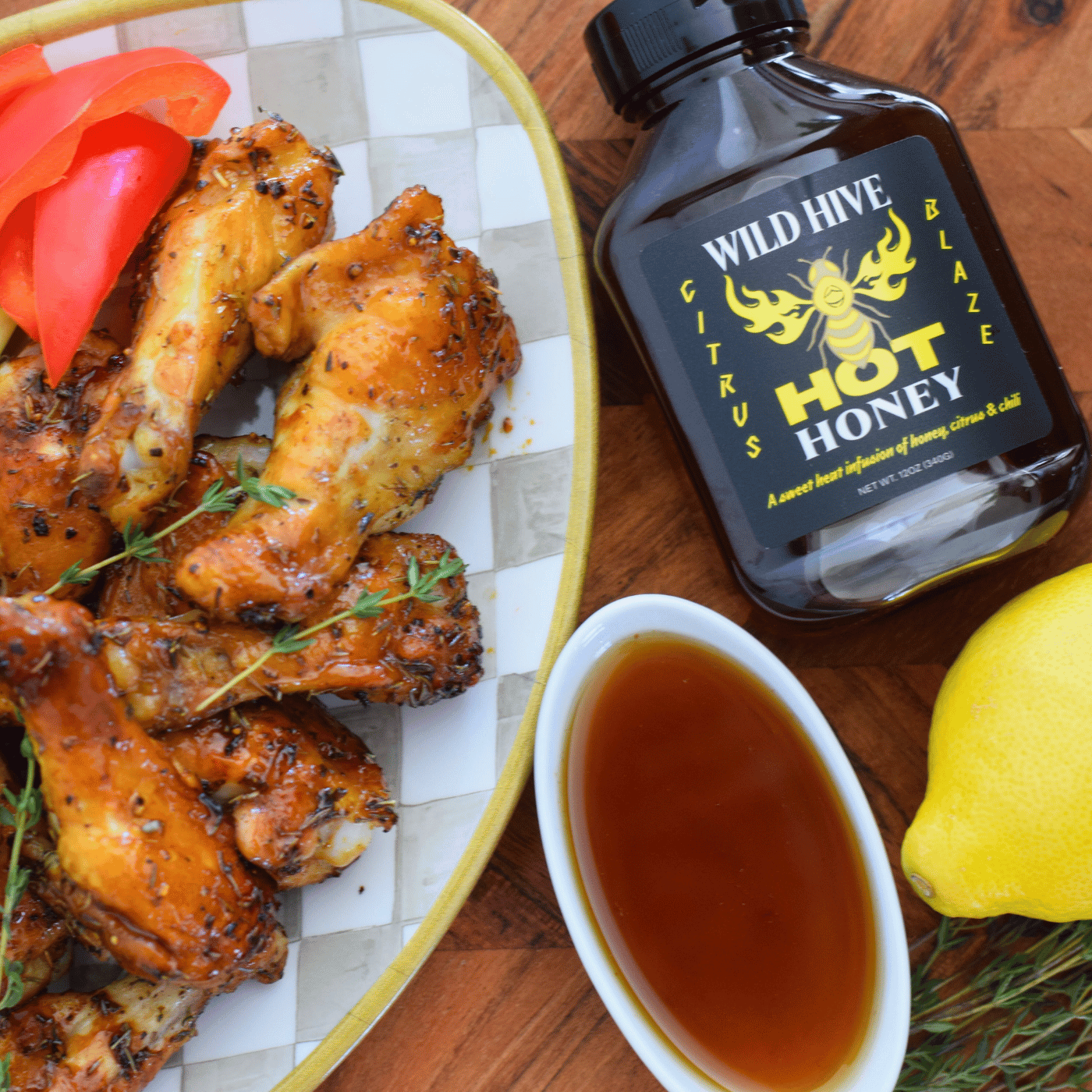 Baked chicken wings with Wild Hive Citrus Blaze Hot Honey, lemon, and a bowl of honey on a wooden surface.