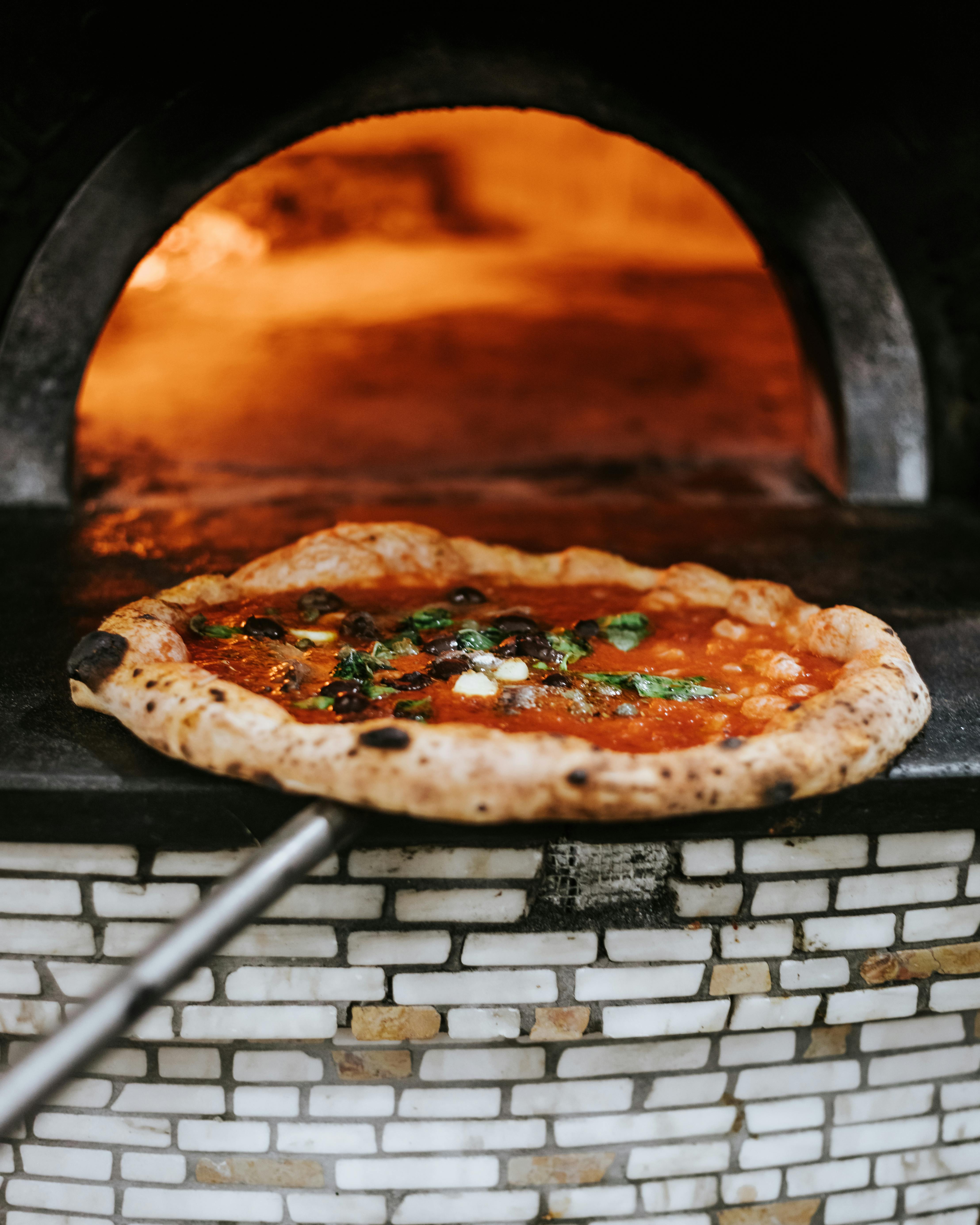 Neapolitan pizza being taken out of a wood-fired oven with a white and beige mosaic pattern on the base.